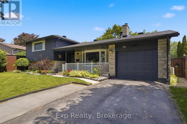 Entrance porch with stone and siding, a glass front door, white railing, and potted plants with red flowers. - 70 Tripp Boulevard, Quinte West