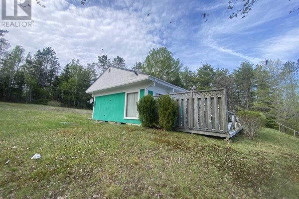 Exterior of a green cottage with white trim, a wooden deck, and a propane tank on the side. - 70 Whispering Pines Lane, North Range