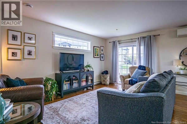 Living room with hardwood floors, sofa, armchair, and entertainment console with TV. - 700 Cliffe Street Unit# 112, Fredericton