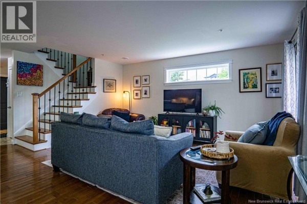 Living room with hardwood floors, sofa, armchair, stairs, and entertainment console with TV. - 700 Cliffe Street Unit# 112, Fredericton