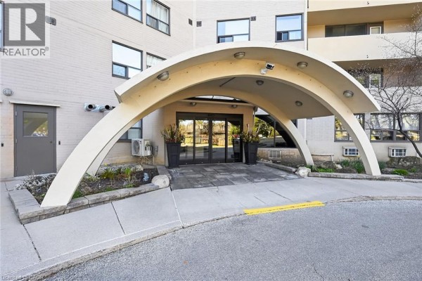 Covered building entrance with large arched canopy, glass doors, and planters. - 700 Dynes Road Unit# 904, Burlington