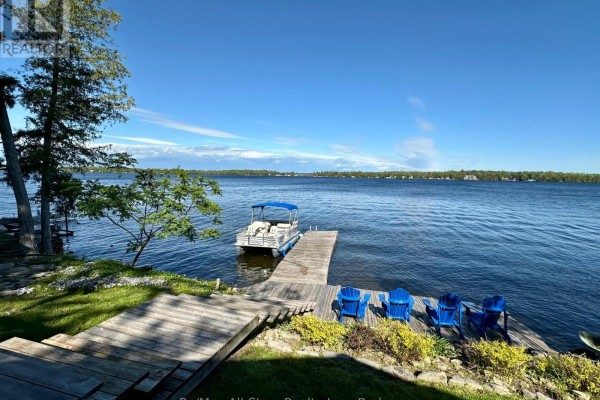 View of a wide blue lake with a pontoon boat docked at a wooden pier. - 700 Grand Island Road, Kawartha Lakes
