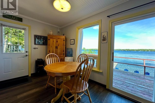 Dining area with a wooden table and chairs, next to a sliding glass door overlooking the water. - 700 Grand Island Road, Kawartha Lakes
