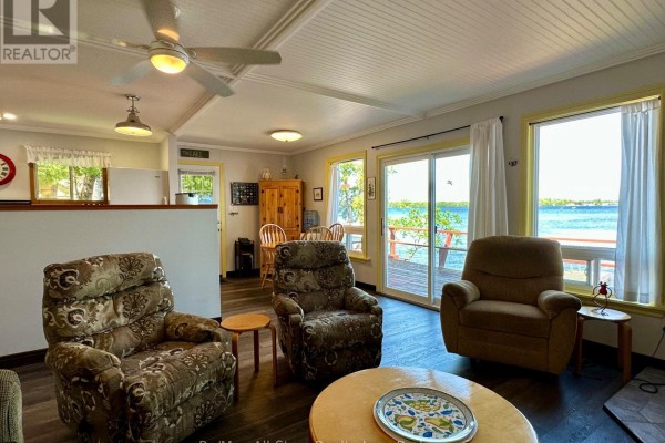 Living area with floral armchairs and a wooden table, with a view of the dining area and lake. - 700 Grand Island Road, Kawartha Lakes