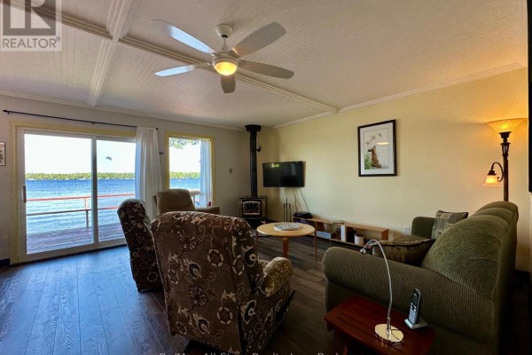 Living room with a green sofa, patterned armchairs, wood stove, and sliding glass doors to the deck. - 700 Grand Island Road, Kawartha Lakes