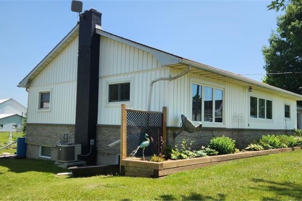 Close-up rear view of the white house showing siding, chimney, air conditioning unit, and raised garden bed. - 700 Norfolk County Rd 28, Langton