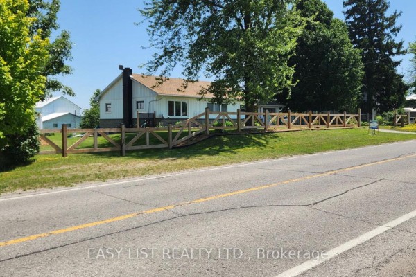 Side view of a white house with a chimney, surrounded by trees and a wooden fence. - 700 Norfolk County Road 28, Norfolk