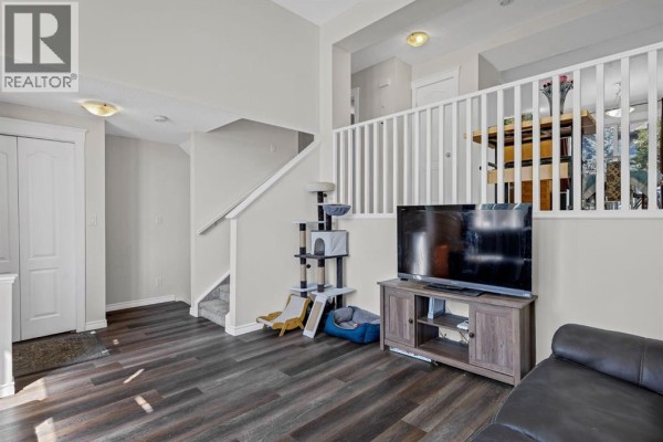 Living room featuring a staircase with white railing, television stand, and plush carpeting. - 7008, 2370 Bayside Road Sw, Airdrie