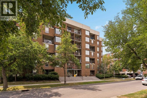 Street view of a large brick apartment building entrance with trees lining the sidewalk. - 701, 1123 13 Avenue Sw, Calgary
