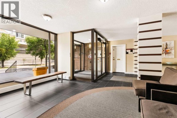 Building lobby with glass doors, tile flooring, a seating area, and brick accent walls. - 701, 1123 13 Avenue Sw, Calgary