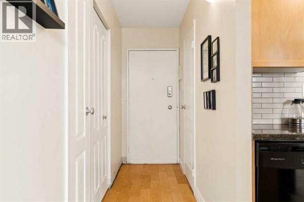 Interior hallway with a white door, hardwood floors, and a partial view of a kitchen. - 701, 1123 13 Avenue Sw, Calgary