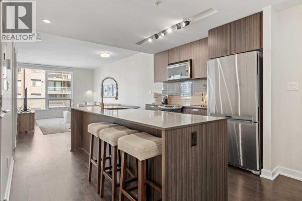 View of an apartment kitchen with an island, bar stools, and stainless steel appliances. - 701, 626 14 Avenue Sw, Calgary