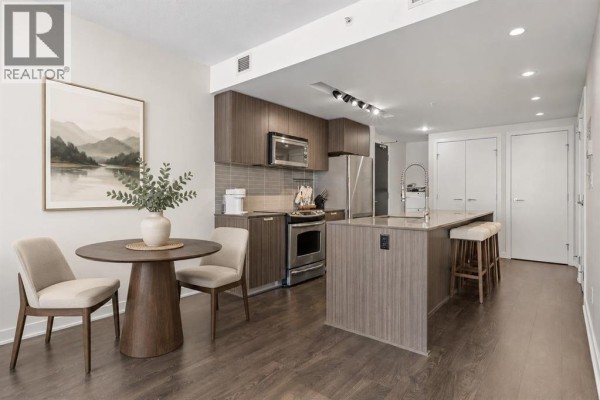 Apartment interior showing a kitchen island with bar stools and a dining table. - 701, 626 14 Avenue Sw, Calgary