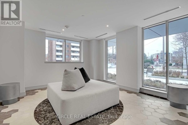 Building lobby with a large white sectional sofa, geometric floor tiles, and large windows. - 701 - 1 Cardiff Road, Toronto