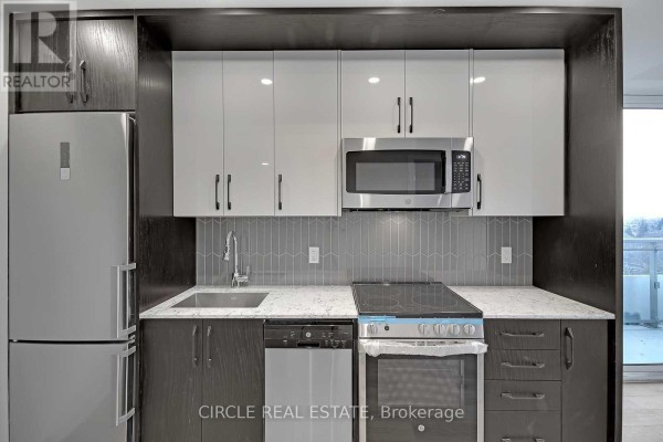 Compact kitchen with stainless steel appliances, grey backsplash, and two-tone cabinetry. - 701 - 1 Cardiff Road, Toronto