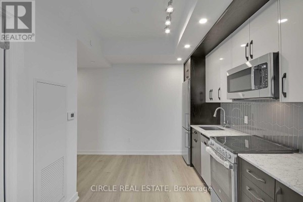 Kitchenette with stainless steel appliances, grey tile backsplash, and light wood flooring. - 701 - 1 Cardiff Road, Toronto
