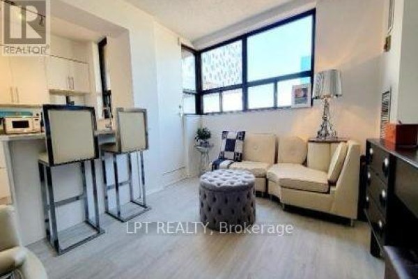 Living room with beige sofa and chairs, a grey tufted ottoman, and a large window. - 701 - 105 Mccaul Street, Toronto