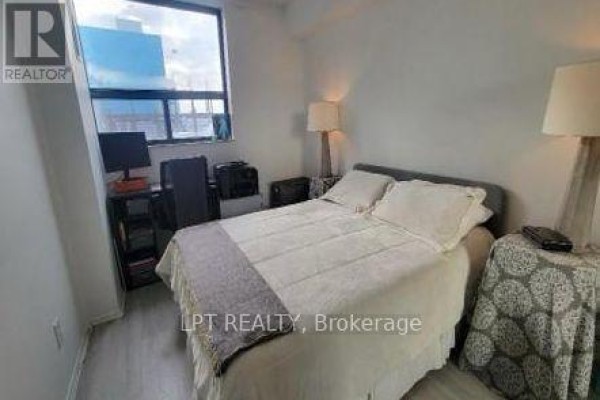 Bedroom with a queen-size bed, grey bedding, two bedside tables, and a desk with a computer. - 701 - 105 Mccaul Street, Toronto
