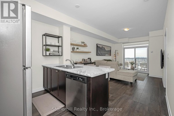 Open-concept living area with kitchen island, stainless steel appliances, and large windows. - 701 - 450 Dundas Street E, Hamilton