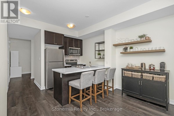Kitchen area with dark cabinetry, bar seating, and stainless steel appliances. - 701 - 450 Dundas Street E, Hamilton