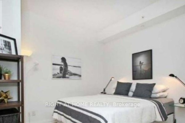 Bedroom with a bed, pillows, artwork, and a shelf with decorative items against a white wall. - 701 - 50 Town Centre Court, Toronto