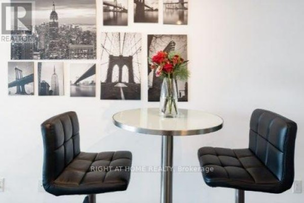 Small dining area with a round table, two black bar stools, and a wall collage of cityscapes. - 701 - 50 Town Centre Court, Toronto