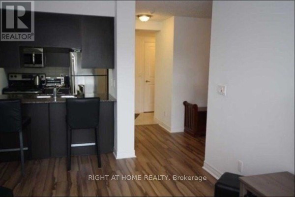 Kitchenette with dark counters, stainless steel appliances, and a hallway leading to a closed door. - 701 - 50 Town Centre Court, Toronto