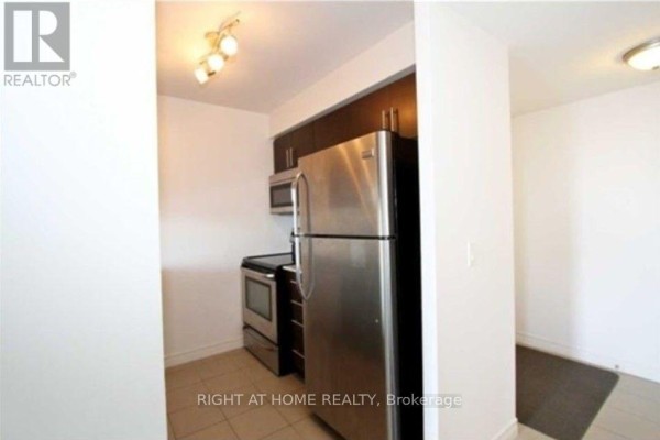 Kitchen area with stainless steel refrigerator, oven, microwave, and dark cabinetry against a tiled floor. - 701 - 50 Town Centre Court, Toronto