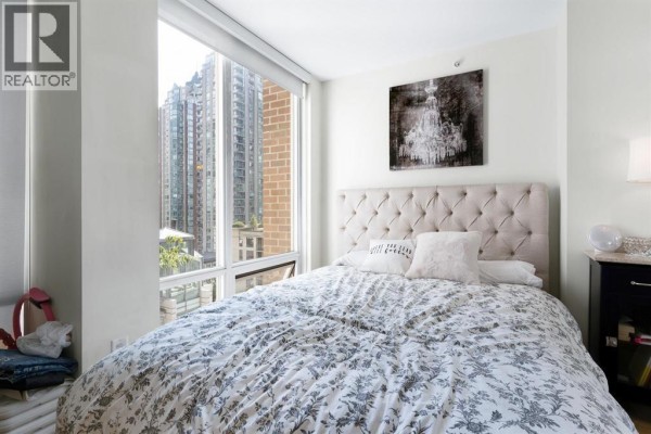Bedroom with a tufted headboard bed and a large window overlooking city buildings. - 701 565 Smithe Street, Vancouver