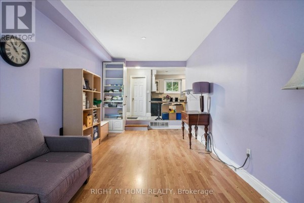 Living room with purple walls, sofa, bookshelf, and kitchen view - 701 Central Park Boulevard N Oshawa