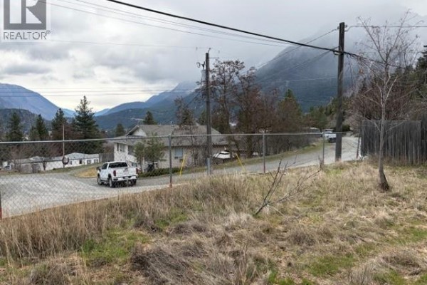 Open lot with grass and a view of the surrounding mountains and nearby road. - 701 Columbia Street, Lillooet