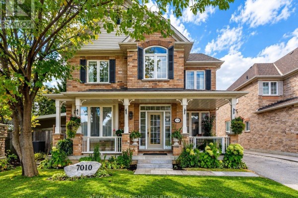 Front exterior of a brick house with a covered porch, large windows, and landscaping. - 7010 Gooderham Estate Boulevard, Mississauga