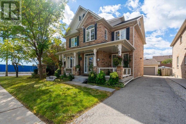 Side exterior view of a brick house with a large lawn, driveway, and nearby garage. - 7010 Gooderham Estate Boulevard, Mississauga