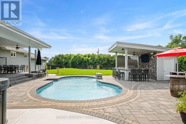 Outdoor living space with a pool, bar, patio, and green lawn on a sunny day. - 7019 Cosgrove Avenue, Ottawa