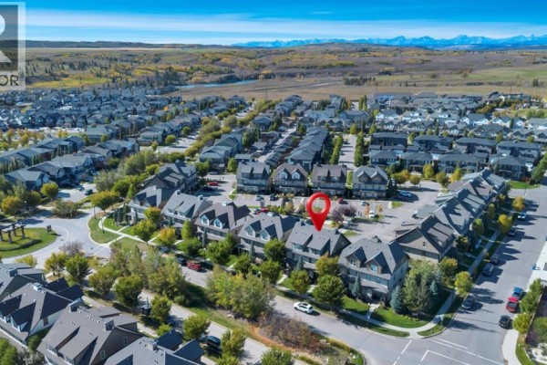 Aerial view of a suburban neighborhood with townhouses and distant mountains under a blue sky. - 702, 50 Belgian Lane, Cochrane