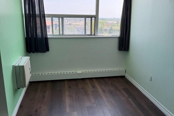 A bedroom with pale green walls, dark wood floors, and a large window covered by a sheer curtain. - 702 - 530 Lolita Gardens, Mississauga