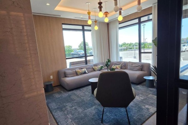 Lobby with a modern fireplace, sectional sofa, armchair, coffee table, and large windows with greenery view. - 702 - 740 Whitlock Avenue, Milton
