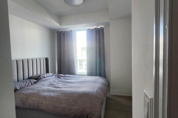 Bedroom with a king-size bed, grey upholstered headboard, and grey curtains framing a window. - 702 - 8 Rouge Valley Drive W, Markham