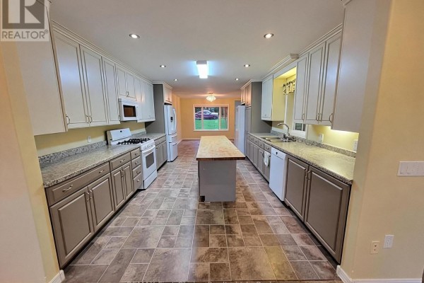 Long kitchen with light grey cabinets, granite countertops, white appliances, and a large central island. - 702 River Avenue E, Rainy River