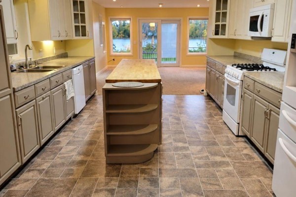 Kitchen with two-tone cabinets, butcher block island, stainless steel sink, and view of dining area. - 702 River Avenue E, Rainy River