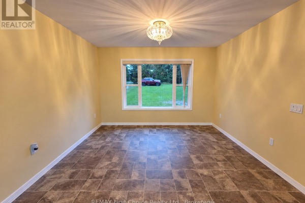 Empty room with yellow walls, beige tiled floor, and a large window overlooking a grassy field. - 702 River Avenue E, Rainy River