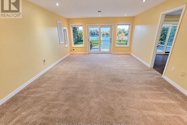 Living room with beige carpet, large windows, and sliding glass doors opening to a balcony with lake view. - 702 River Avenue E, Rainy River