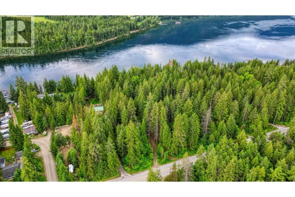Aerial view showing a forested property with a lake, a road, and several mobile homes. - 7022 Highway 3a, Balfour