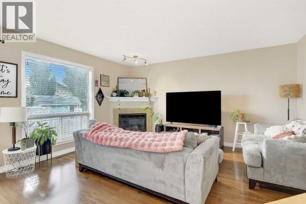Living room with a gray sofa, fireplace, large window, and hardwood floors. - 7025 112 Street, Grande Prairie
