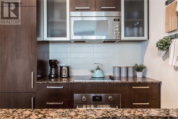 Kitchen sink area with granite counter, subway tile backsplash, and wall-mounted pots. - 703 - 12 York Street, Toronto