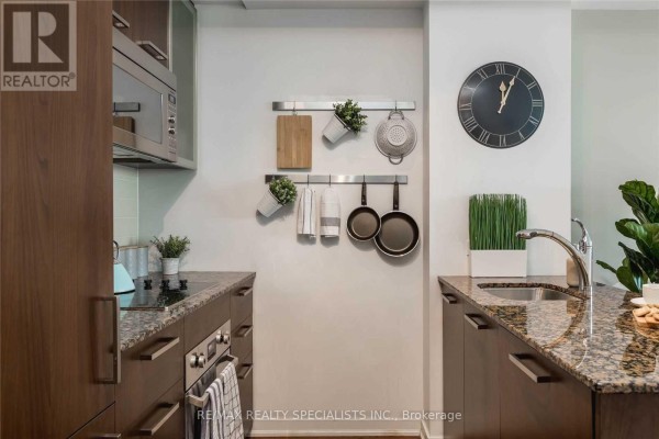 Compact kitchen with granite countertops, stainless steel appliances, and dark wood cabinetry. - 703 - 12 York Street, Toronto