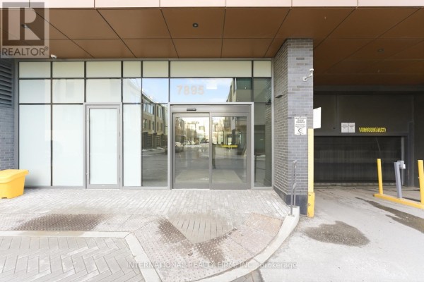 Building entrance with glass doors, metal framing, and an adjacent parking garage entrance. - 703 - 7895 Jane Street, Vaughan