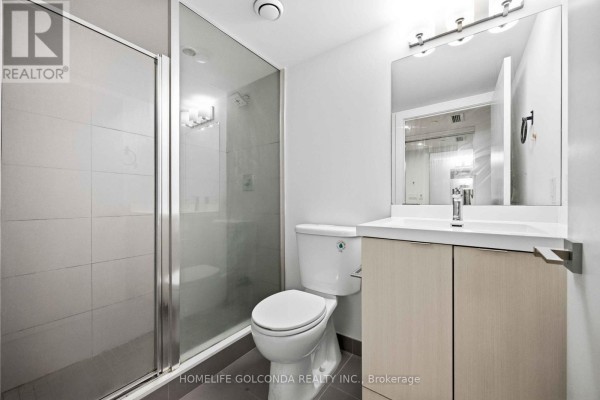 Living area with white sofa, dark wood floors, and view of city buildings through glass sliding doors. - 703 - 89 Mcgill Street, Toronto