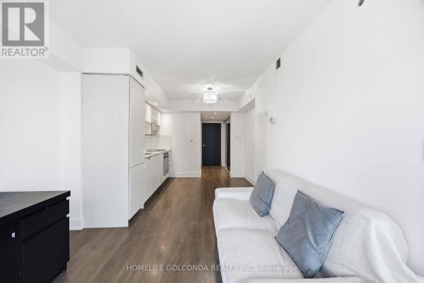 View of the open-concept living space, including a white sofa and a galley kitchen with light wood cabinets. - 703 - 89 Mcgill Street, Toronto