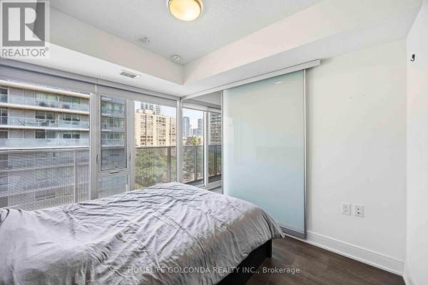 Bedroom with a grey duvet on the bed, a sliding frosted glass door, and a city view from the windows. - 703 - 89 Mcgill Street, Toronto